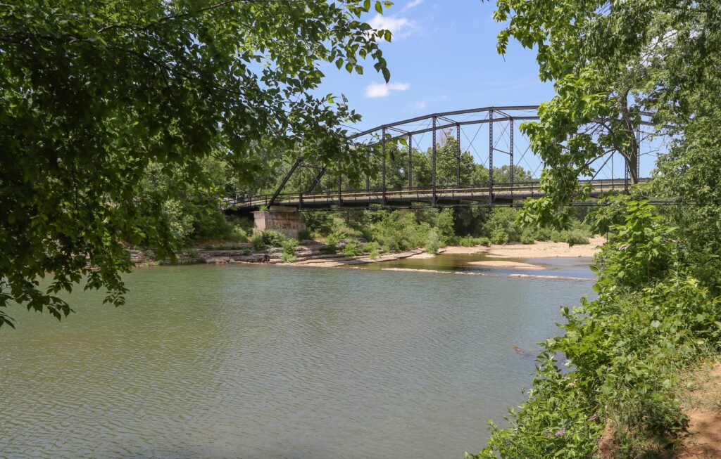 A picturesque view of War Eagle Bridge spanning a serene river surrounded by lush greenery in Arkansas.