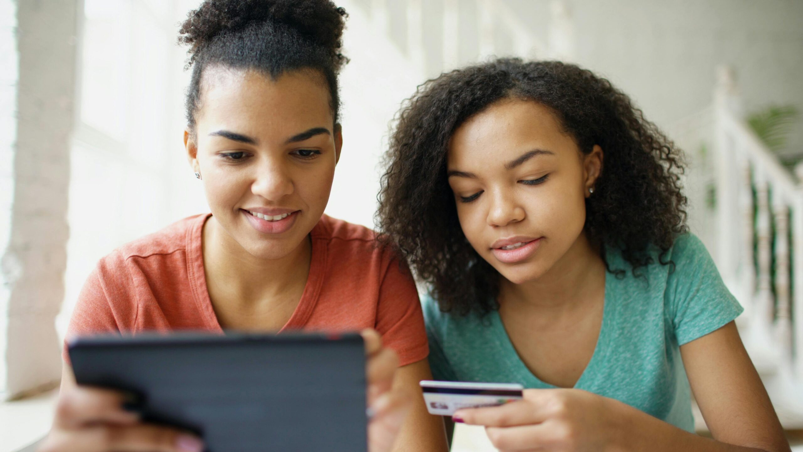Two women using a tablet and credit card to shop online, displaying modern lifestyle indoors.